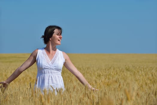 Young woman standing jumping and running  on a wheat field with blue sky the background at summer day representing healthy life and agriculture concept