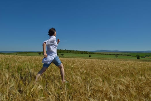 Young woman standing jumping and running  on a wheat field with blue sky the background at summer day representing healthy life and agriculture concept