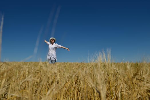 Young woman standing jumping and running  on a wheat field with blue sky the background at summer day representing healthy life and agriculture concept