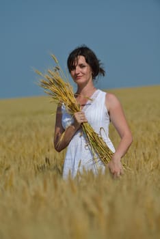 Young woman standing jumping and running  on a wheat field with blue sky the background at summer day representing healthy life and agriculture concept