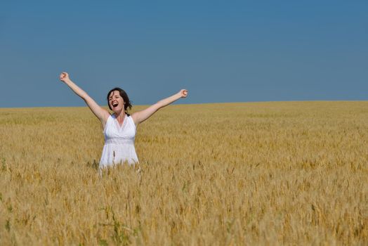 Young woman standing jumping and running  on a wheat field with blue sky the background at summer day representing healthy life and agriculture concept