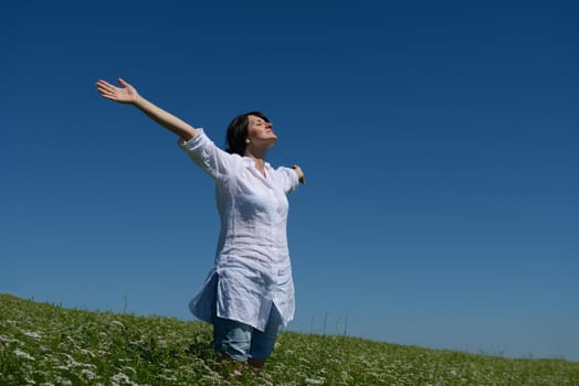 Young happy woman in green field with blue sky in background