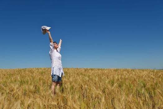 Young woman standing jumping and running  on a wheat field with blue sky the background at summer day representing healthy life and agriculture concept