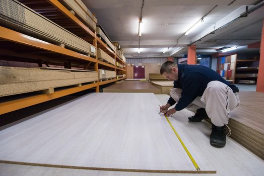 young man carpenter measuring wooden board for cutting while working in big modern carpentry High quality wood concept