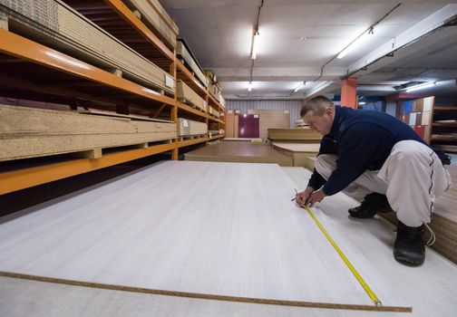 young man carpenter measuring wooden board for cutting while working in big modern carpentry High quality wood concept