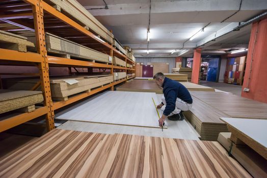 young man carpenter measuring wooden board for cutting while working in big modern carpentry High quality wood concept