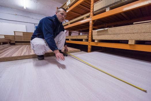 young man carpenter measuring wooden board for cutting while working in big modern carpentry High quality wood concept