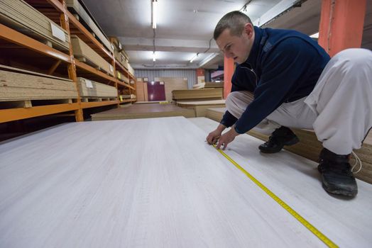 young man carpenter measuring wooden board for cutting while working in big modern carpentry High quality wood concept