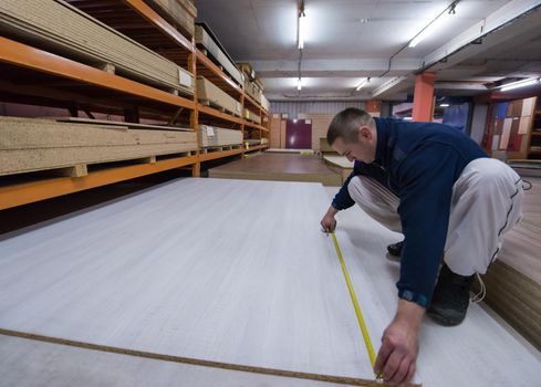 young man carpenter measuring wooden board for cutting while working in big modern carpentry High quality wood concept