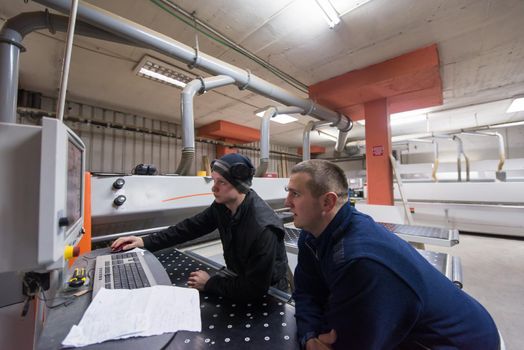 two young carpenters calculating and programming a cnc wood working machine in workshop. wood workers preparing a computer program for CNC machine at big modern carpentry