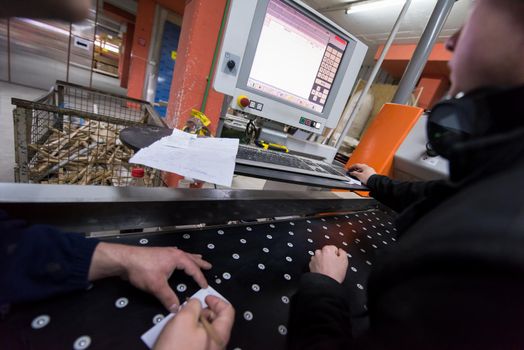 two young carpenters calculating and programming a cnc wood working machine in workshop. wood workers preparing a computer program for CNC machine at big modern carpentry