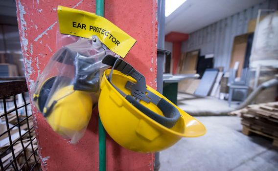 standard security equipment yellow helmet and ears protection hanging on the wall at production Department of a big modern wooden furniture factory
