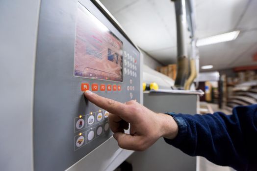 young carpenter calculating and programming a cnc wood working machine in workshop. wood worker preparing a computer program for CNC machine at big modern carpentry