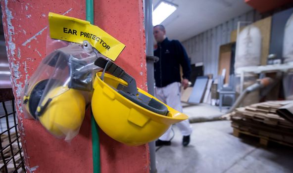 standard security equipment yellow helmet and ears protection hanging on the wall at production Department of a big modern wooden furniture factory