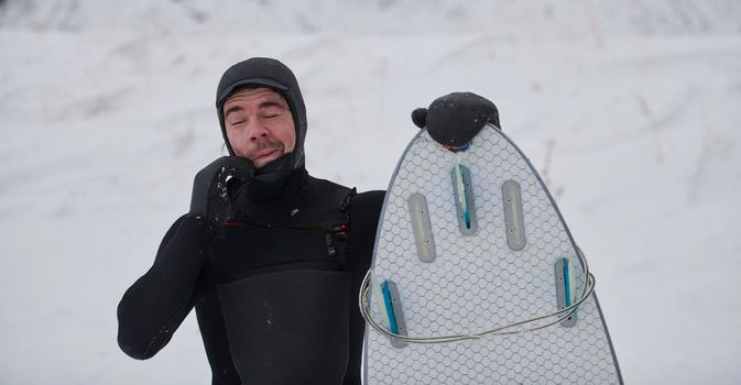 Authentic local Arctic surfer portrait holding a board after surfing in Norwegian sea. Snow capped mountain background. Winter water activities extreme sport