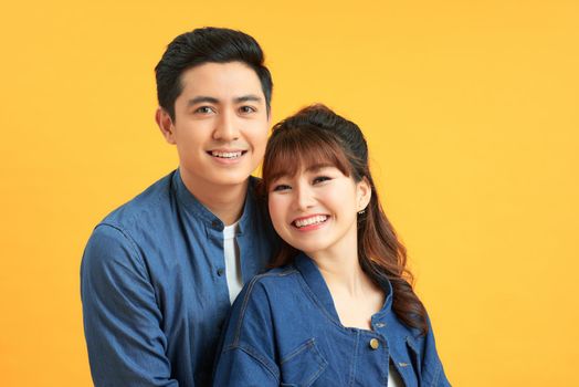 Portrait of joyful asian couple embracing over yellow studio background