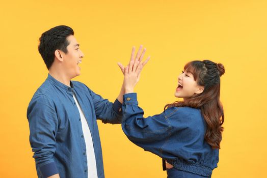 Portrait of a cheery young couple giving high five over yellow background