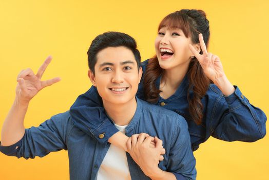 Portrait of joyful asian couple embracing over yellow studio background