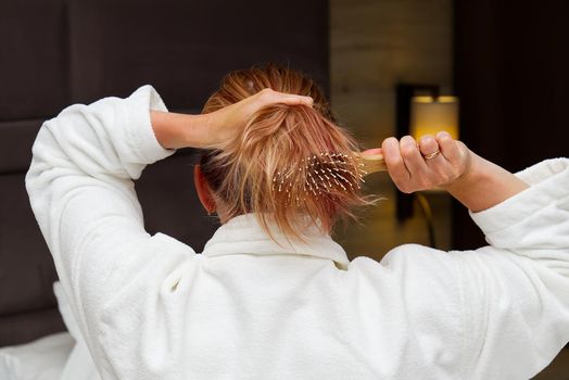 a blonde with dyed hair combing her tangled hair after a shower with a wooden comb. close-up