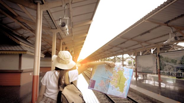 Young Girl Tourist carrying a bag and holding map hitchhiking the train on the railway at the train station. Concept of travel and tourism.