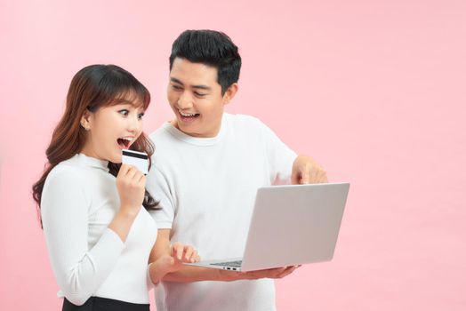 Excited young couple shopping online, holding credit card and looking at laptop 