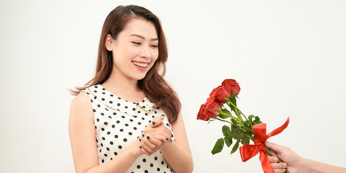 A cute surprised enthusiastic girl stands next to a young handsome guy who gives her a bouquet of red roses. 