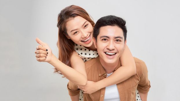 Playful asian happy man piggybacking pretty woman against plain white background