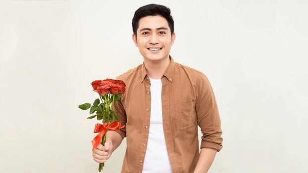 Smiling Asian man holding bunch of roses. Young man looking at camera. Flowers and gift concept. 