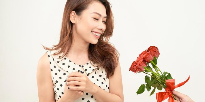 A cute surprised enthusiastic girl stands next to a young handsome guy who gives her a bouquet of red roses. 