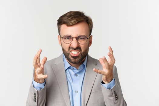 Close-up of angry businessman in gray suit and glasses, shaking hands and grimacing mad, standing over white background.