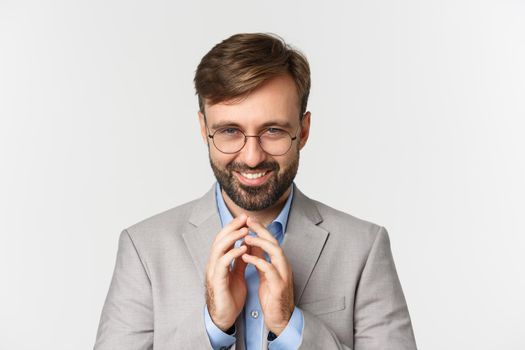 Close-up of bearded businessman in glasses and suit, scheming something, smiling devious and having perfect plan, standing over white background.