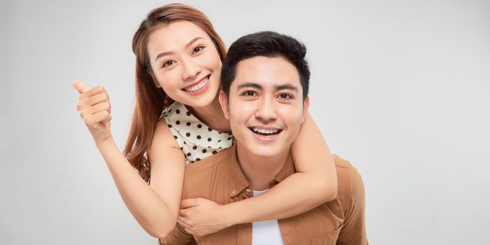 Love forever. Young asian handsome boyfriend is piggybacking his cute lover, wearing casual clothes, on white background
