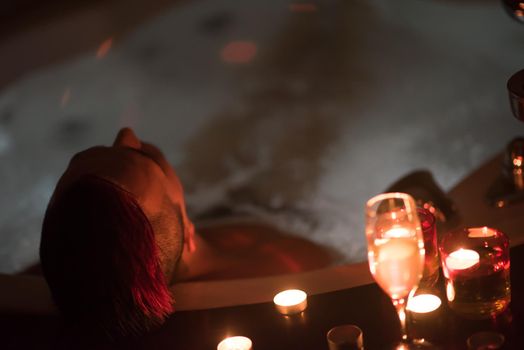 young handsome man enjoys relaxing in the jacuzzi with candles and champagne at luxury resort spa