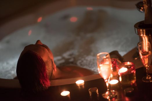 young handsome man enjoys relaxing in the jacuzzi with candles and champagne at luxury resort spa