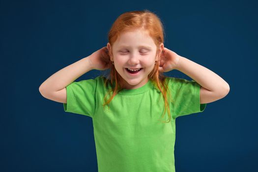 close up photo of little redhead emotional girl in green t-shirt posing before camera.She is tired and wants to sleep, yawning and stretching