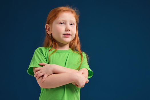 close up photo of little redhead emotional girl in green t-shirt posing before camera. She shows mistrust and shyness