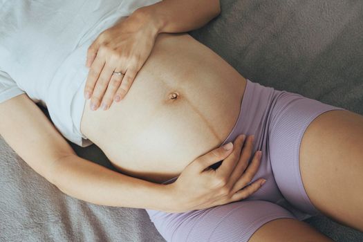 Pregnant caucasian woman laying on a sofa with her arms at tummy, view from the top.