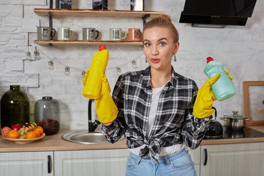 Woman comparing detergent products, she is holding two bottles and checking them at home kitchen. Household, cleaning and people concept