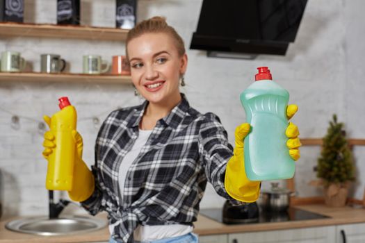 Woman comparing detergent products, she is holding two bottles and checking them at home kitchen. Household, cleaning and people concept