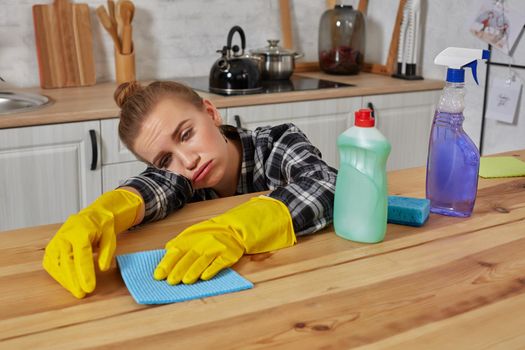 Young woman in protective gloves wipes a table in the kitchen with a rag. Fatigue. Household, cleaning and people concept