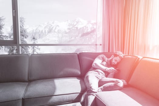 young man sitting on sofa and using a mobile phone  near the window at home