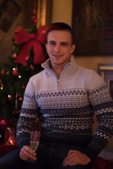 Portrait of a happy young man with a glass of champagne celebrating winter holidays at home beautifully decorated for Christmas