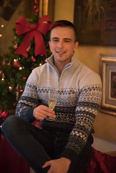 Portrait of a happy young man with a glass of champagne celebrating winter holidays at home beautifully decorated for Christmas