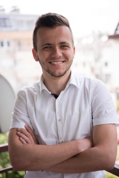 young elegant fashion man standing at balcony with arms crossed and smiling