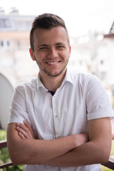 young elegant fashion man standing at balcony with arms crossed and smiling