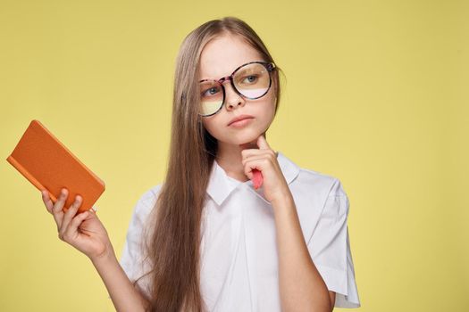 schoolgirl with textbook in hands learning childhood yellow background. High quality photo