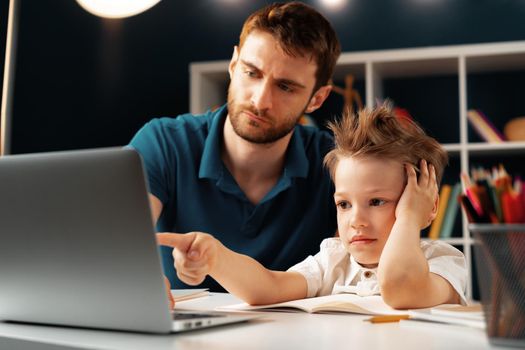 Young boy sitting with his father at the table and using laptop for study