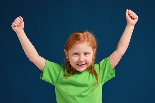 close up photo of little redhead emotional girl in green t-shirt posing before camera.She is tired and wants to sleep, yawning and stretching