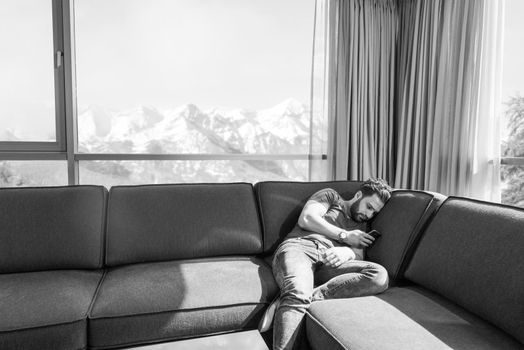 young man sitting on sofa and using a mobile phone  near the window at home