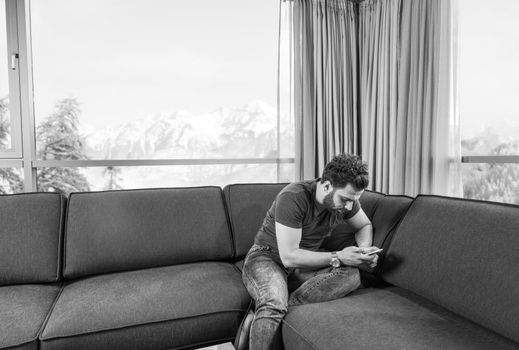 young man sitting on sofa and using a mobile phone  near the window at home